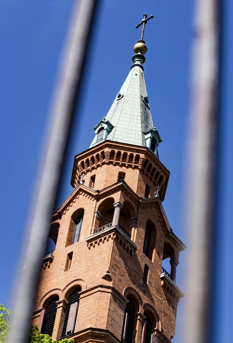 Brick church steeple topped with a cross seen between blurred metal bars
